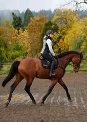 Woman riding a horse in an outdoor arena while wearing the Kerrits Microcord Knee Patch Pocket Tight in black