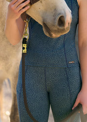 Close-up of model wearing blue printed riding tights and matching tank top, standing next to a horse