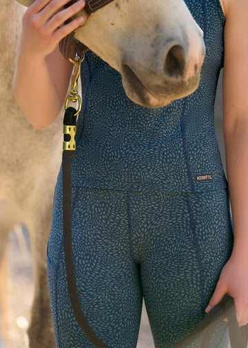 Close-up of model wearing blue printed riding tights and matching tank top, standing next to a horse