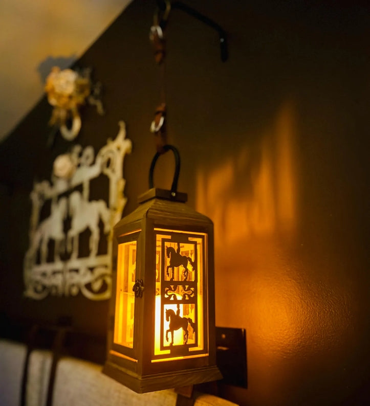 Angled side view of the lit dressage All Designs Equine Horse Lantern hanging on a brown wall