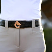 Close-up front view of a model wearing the black side of the Criniere Reversible Pebble Leather Logo Belt over tan breeches