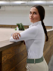 Side view of a female model wearing the white Criniere Monique The Winner's Edge Mesh Show Shirt while leaning against an indoor arena wall