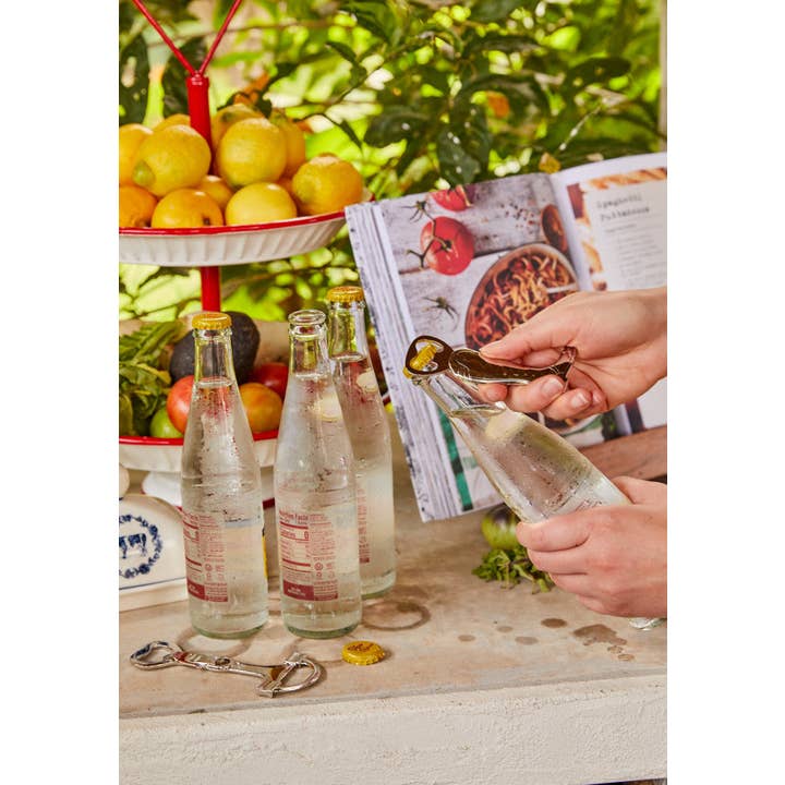 View of someone using the riding boot Blue Stallion Farm Zinc Bottle Opener to open a bottle with a vibrant background