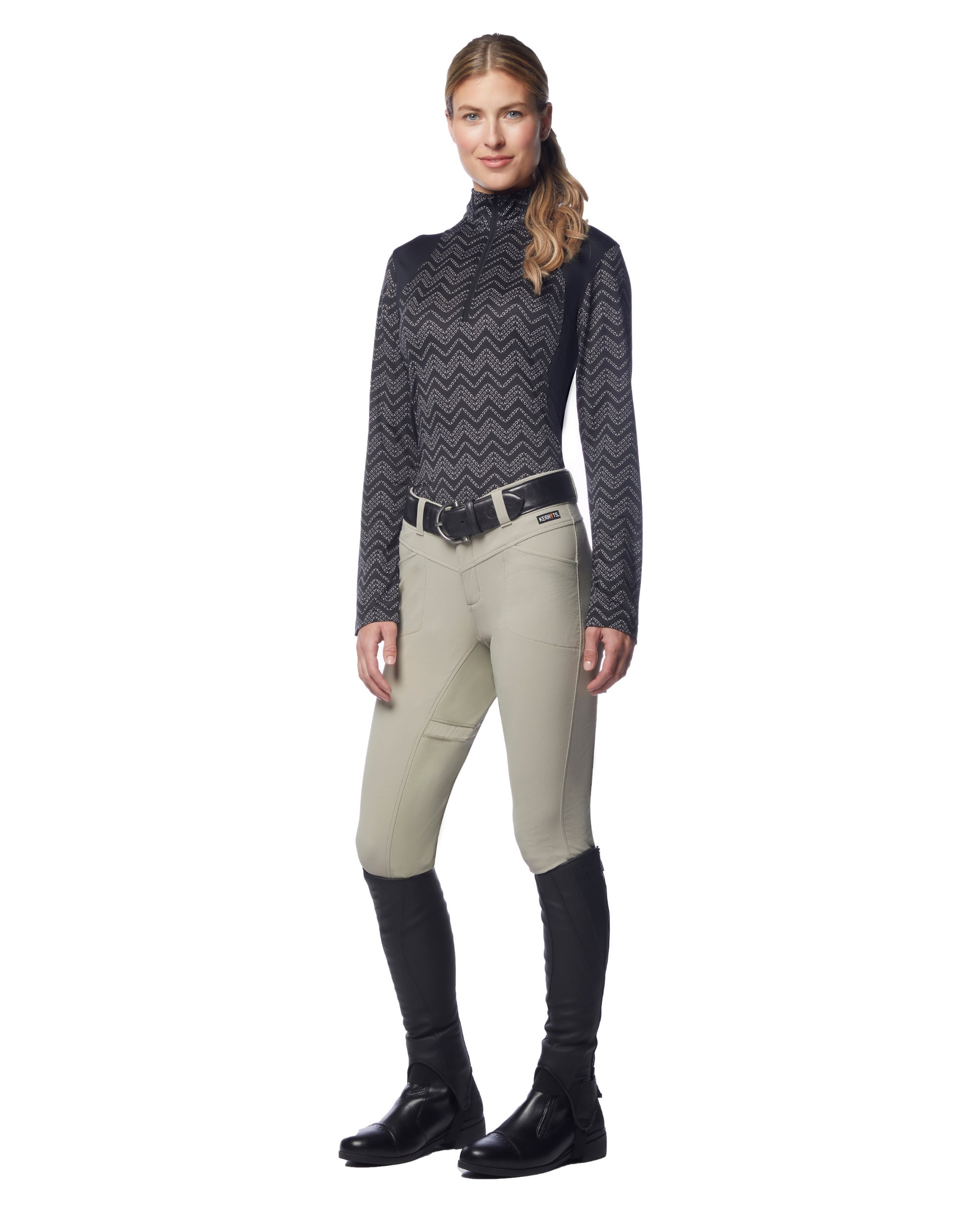 Full body front view of a female model wearing the sand Kerrits Crossover II Full Seat Breech with black patterned shirt on a white background