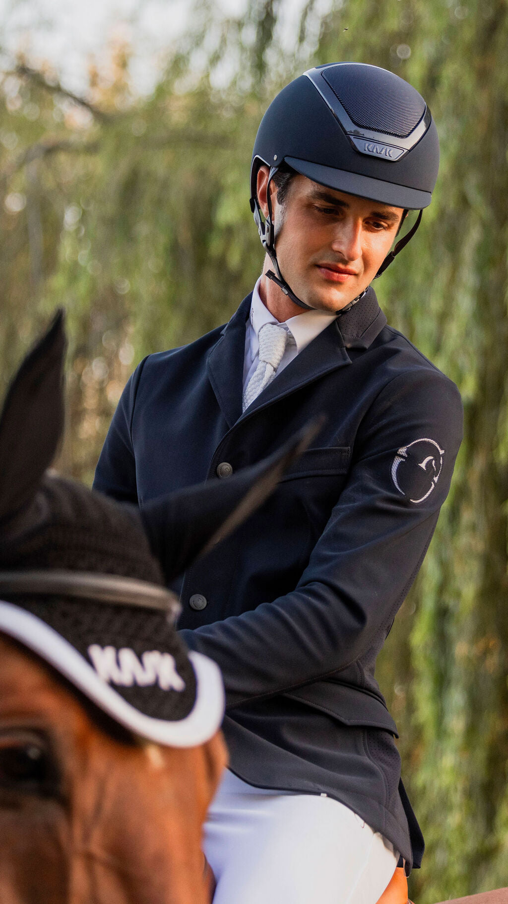 Angled front view of a male model wearing the navy Kask Dogma Chrome Helmet while riding a horse