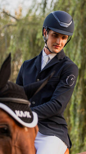 Angled front view of a male model wearing the navy Kask Dogma Chrome Helmet while riding a horse
