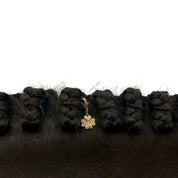 Close-up of a gold clover Dubois Cheval Braid Charm in a black horse's braided mane on a white background