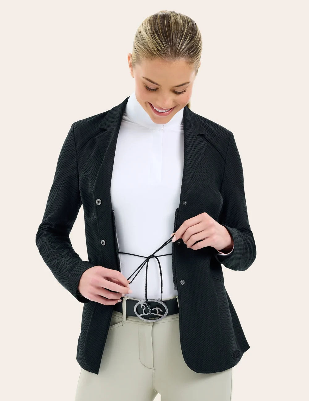 Front view of a female model wearing the black RJ Classic Addison Air Mesh Coat and adjusting the tie on her competition number tabard on a plain background