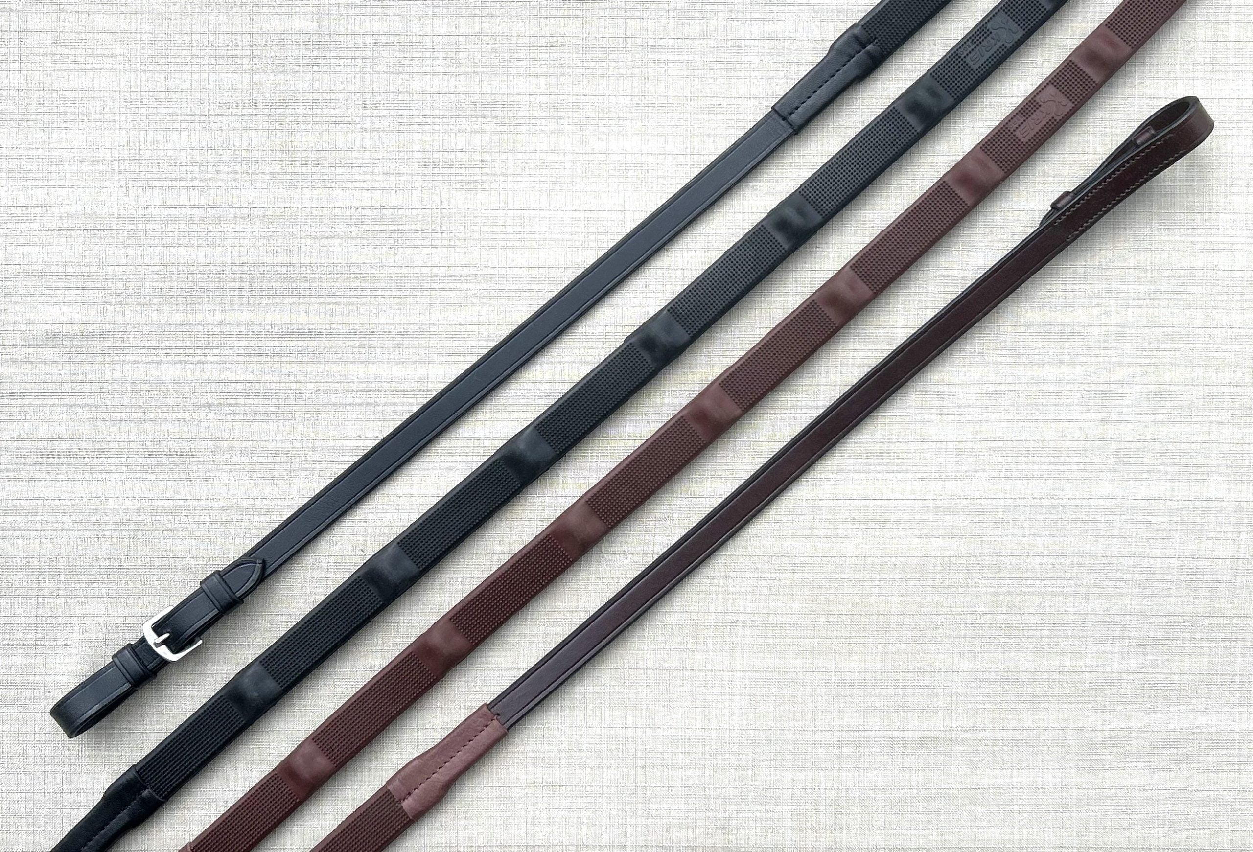 Side-by-side views of black buckle and brown pin pairs of Red Barn Bump Grip Reins on a textured background