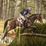 View of a male model jumping a horse over a cross country obstacle while the horse is wearing the black Boyd Martin Eventing 4 Pack