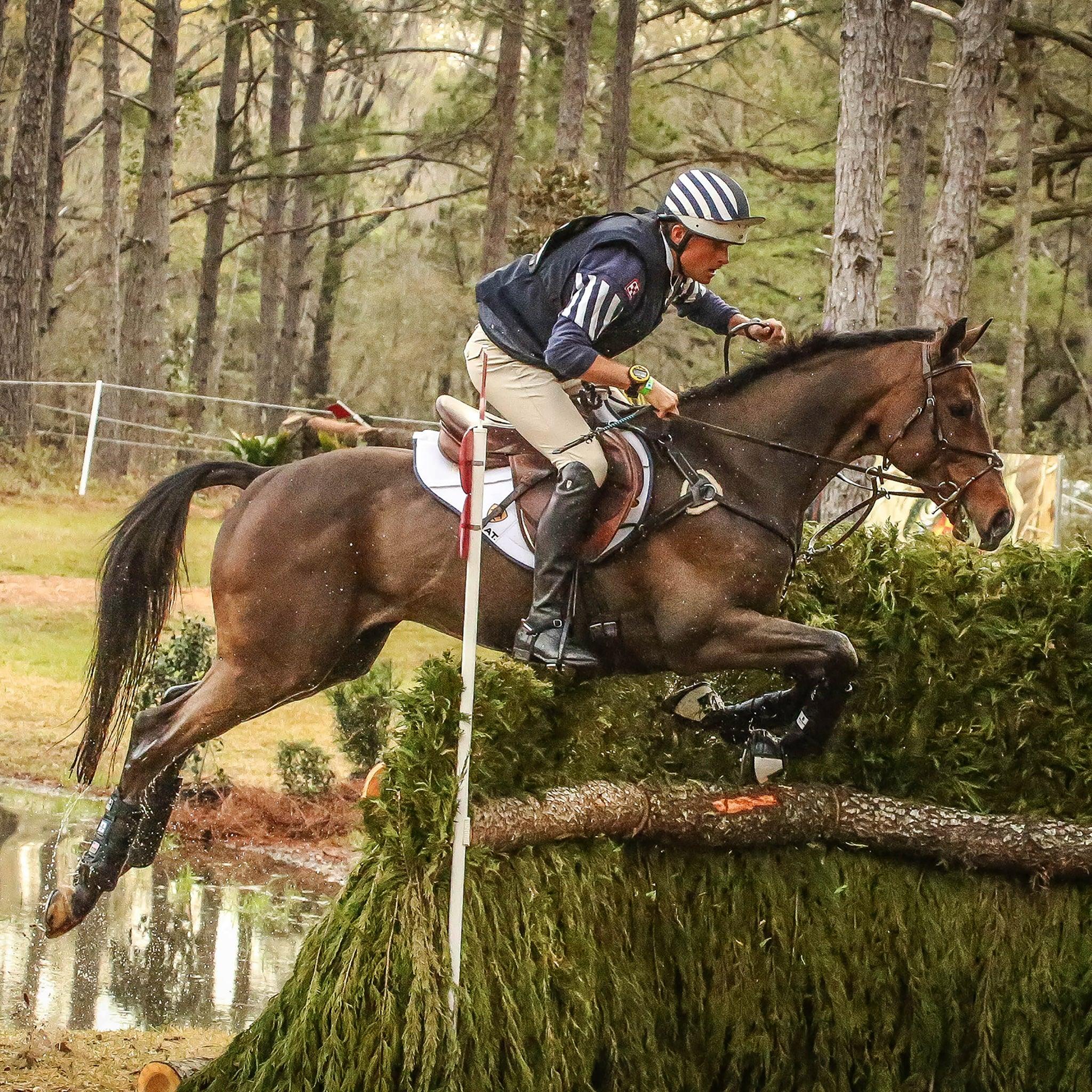 View of a male model jumping a horse over a cross country obstacle while the horse is wearing the black Boyd Martin Eventing 4 Pack