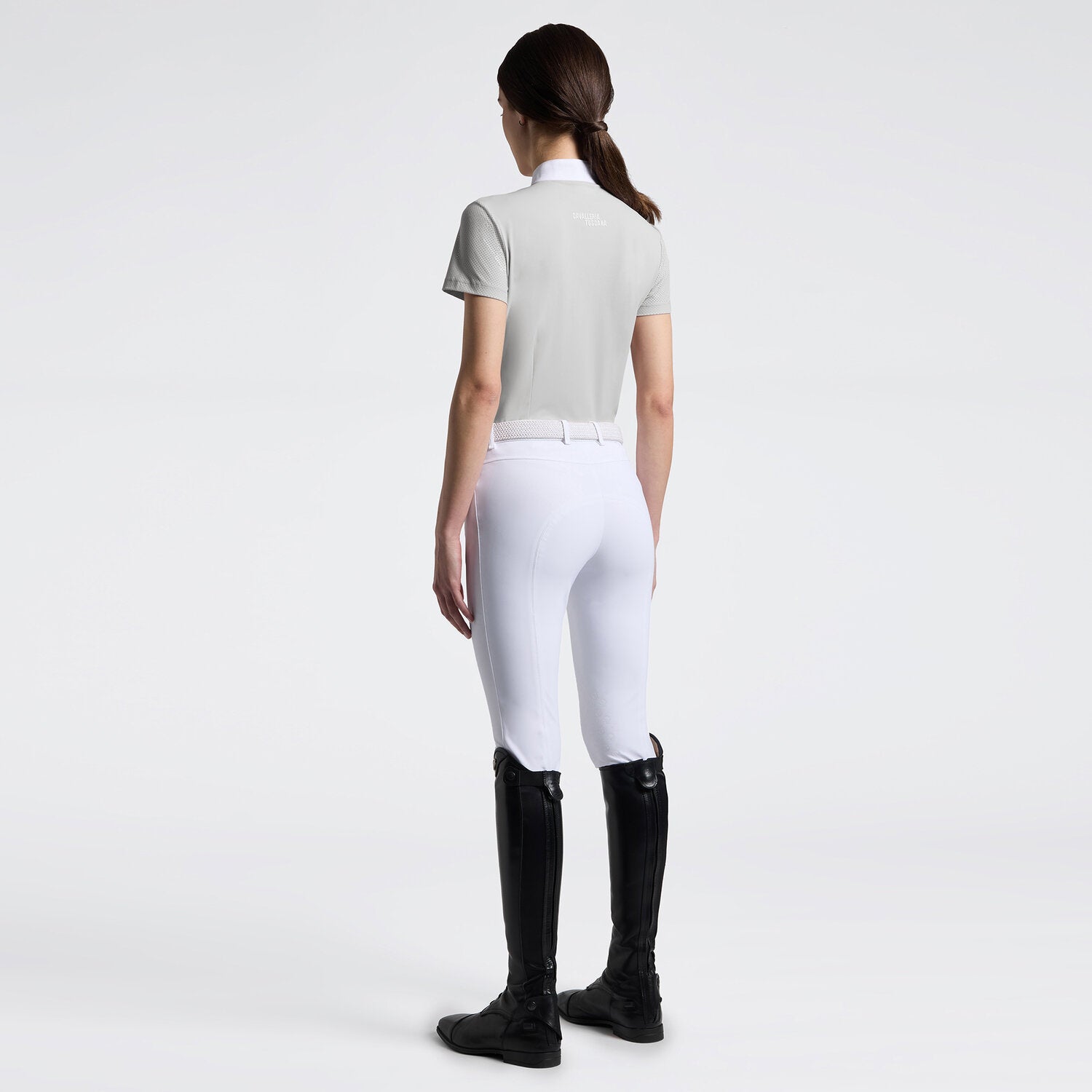 Full body back view of a model wearing the gray Cavalleria Toscana Perforated Short Sleeve Competition Shirt and white breeches on a plain background