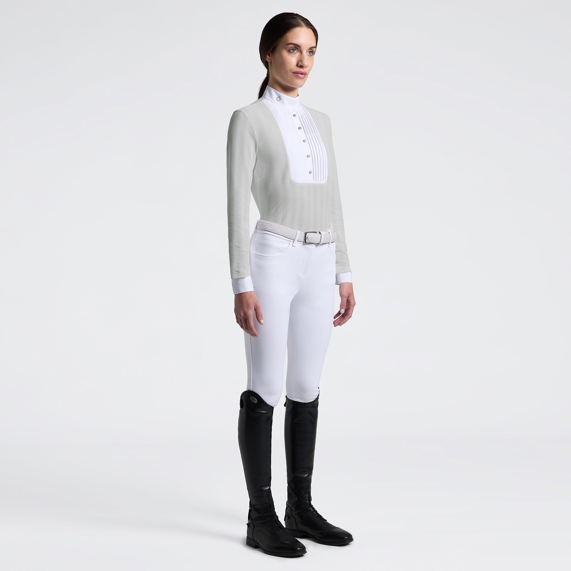 Full body angled front view of a female model wearing the gray Cavalleria Toscana Long Sleeve Jacquard Jersey Competition Shirt with white breeches on a plain background