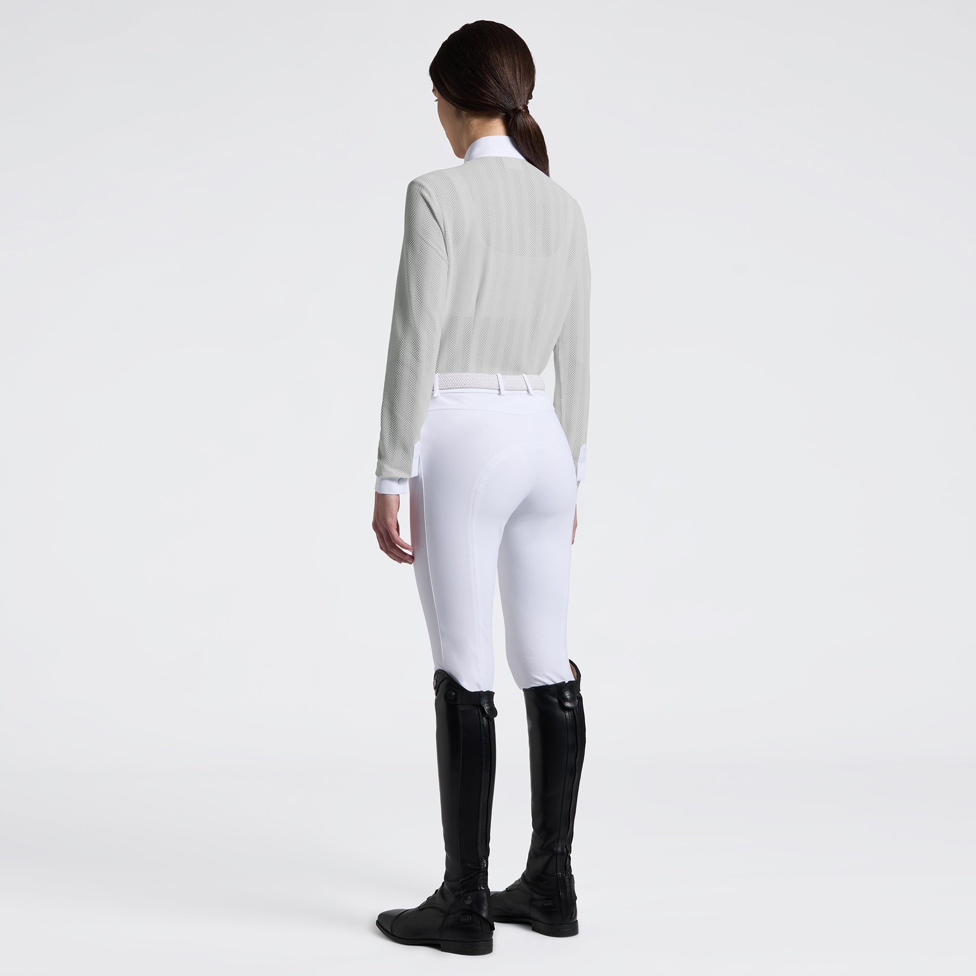 Full body angled back view of a female model wearing the gray Cavalleria Toscana Long Sleeve Jacquard Jersey Competition Shirt with white breeches on a plain background