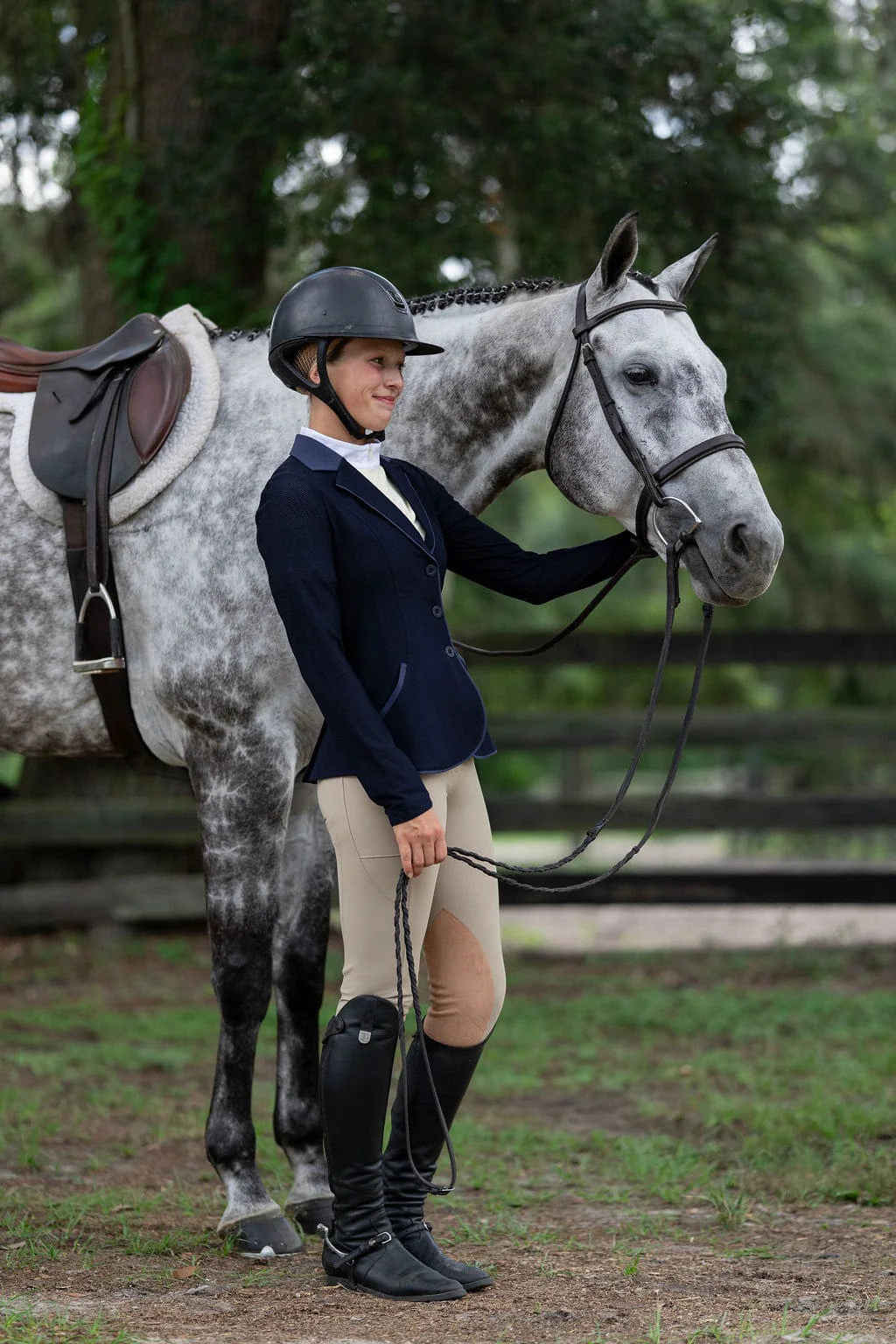 Angled front view of a model wearing the beige Free Ride PRO Knee Patch Breeches while standing in front of a gray horse