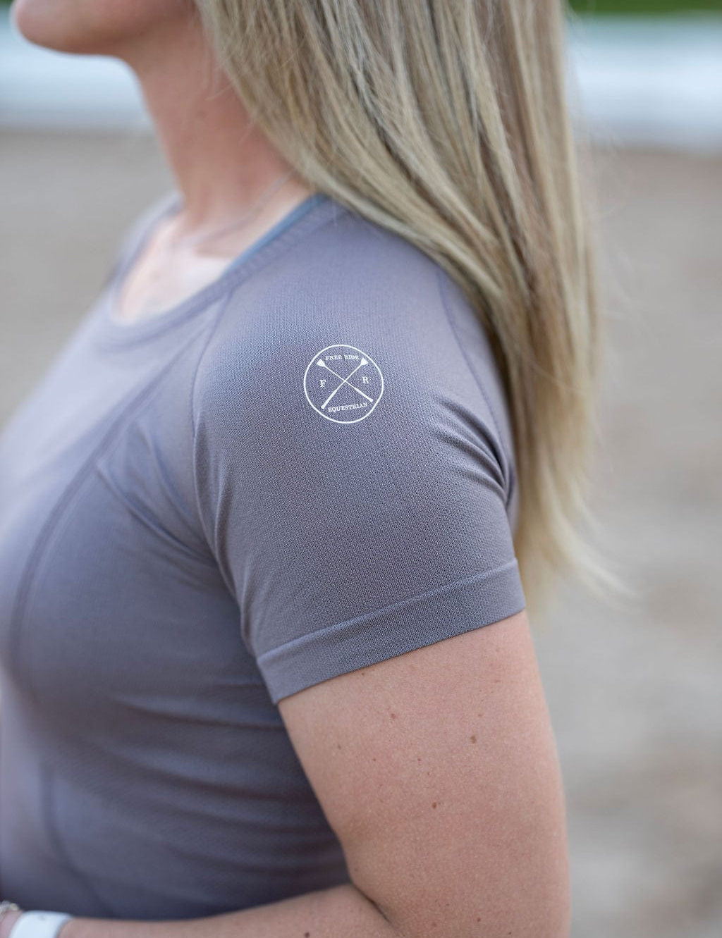 Side view of a female model wearing the Urban Grey Free Ride Seamless Short Sleeve Top while standing in an outdoor arena