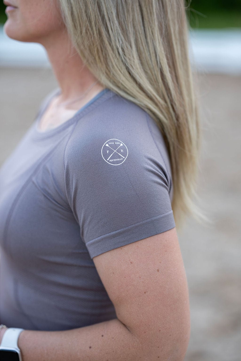 Side view of a female model wearing the Urban Grey Free Ride Seamless Short Sleeve Top while standing in an outdoor arena