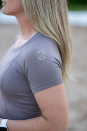 Side view of a female model wearing the Urban Grey Free Ride Seamless Short Sleeve Top while standing in an outdoor arena