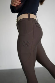 Side view of a female model wearing the brown Free Ride Lux Knee Patch Breeches in a studio setting