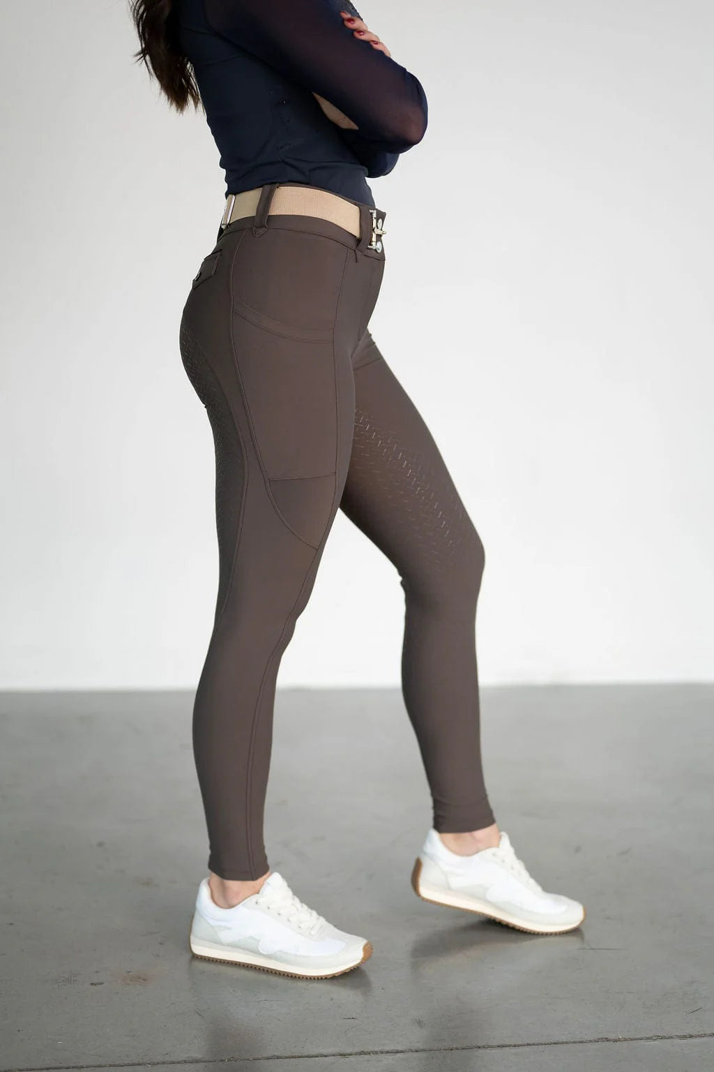 Side view of a female model wearing the brown Free Ride Lux Knee Patch Breeches in a studio setting
