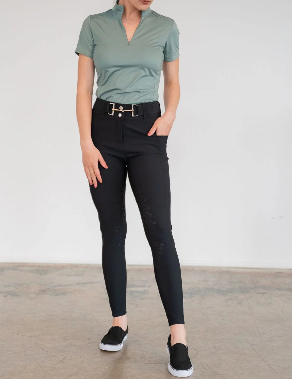 Front view of a model wearing the black Free Ride PRO Knee Patch Breeches and green shirt in a studio setting