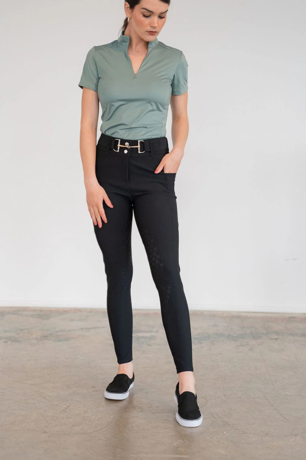 Front view of a model wearing the black Free Ride PRO Knee Patch Breeches and green shirt in a studio setting