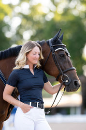 Angled front view of a female model wearing the navy Free Ride Cassidy Short Sleeve Show Shirt while standing next to a bay horse