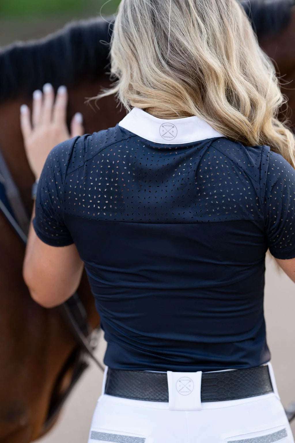 Back view of a female model wearing the navy Free Ride Cassidy Short Sleeve Show Shirt while petting a bay horse's neck