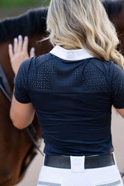 Back view of a female model wearing the navy Free Ride Cassidy Short Sleeve Show Shirt while petting a bay horse's neck
