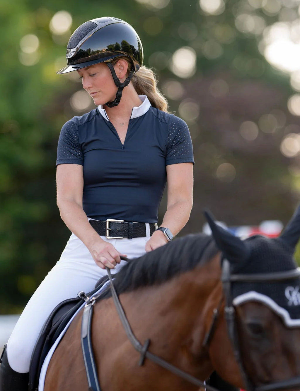 Front view of a female model wearing the navy Free Ride Cassidy Short Sleeve Show Shirt while riding a bay horse