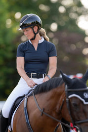 Front view of a female model wearing the navy Free Ride Cassidy Short Sleeve Show Shirt while riding a bay horse