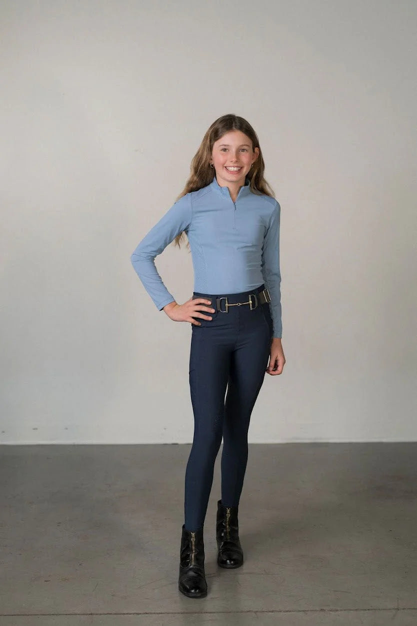 Full body front view of a young model wearing the navy Free Ride Youth Lux Full Seat Breeches and blue top on a plain background
