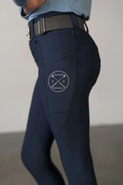 Close-up side view of a young model wearing the navy Free Ride Youth Lux Full Seat Breeches on a plain background