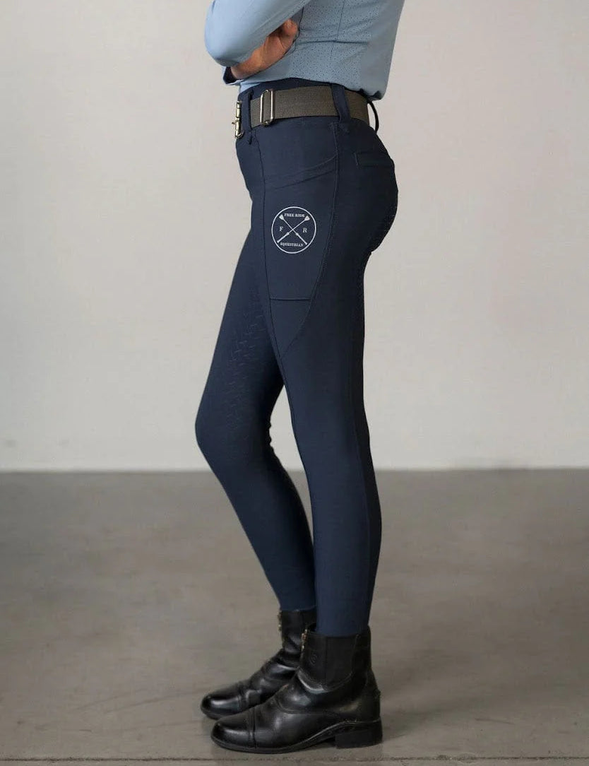 Side view of a young model wearing the navy Free Ride Youth Lux Full Seat Breeches on a plain background