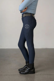 Side view of a young model wearing the navy Free Ride Youth Lux Full Seat Breeches on a plain background