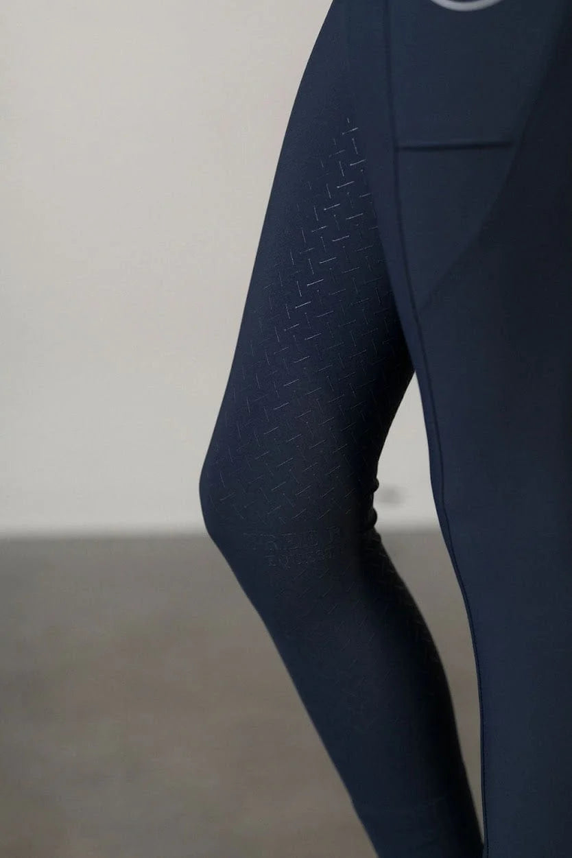 Close-up view of the silicone knee patch on the navy Free Ride Youth Lux Full Seat Breeches on a plain background