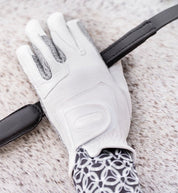 Close-up view of the back of the hand of a model wearing the white Correct Connect Oil-Tac Copper Tech™ Leather Premium Riding Gloves while holding a rein against a gray horse