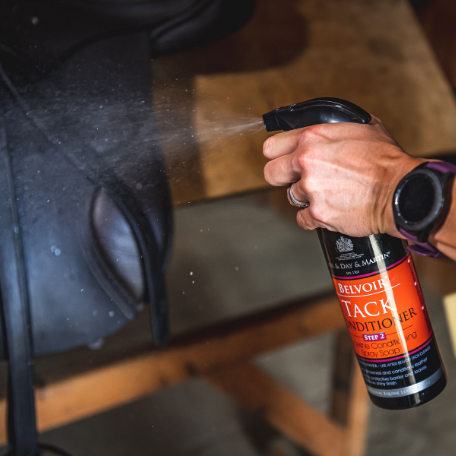 Close-up view of someone spraying a bottle of Carr & Day & Martin Belvoir Tack Conditioner Spray directly onto a saddle