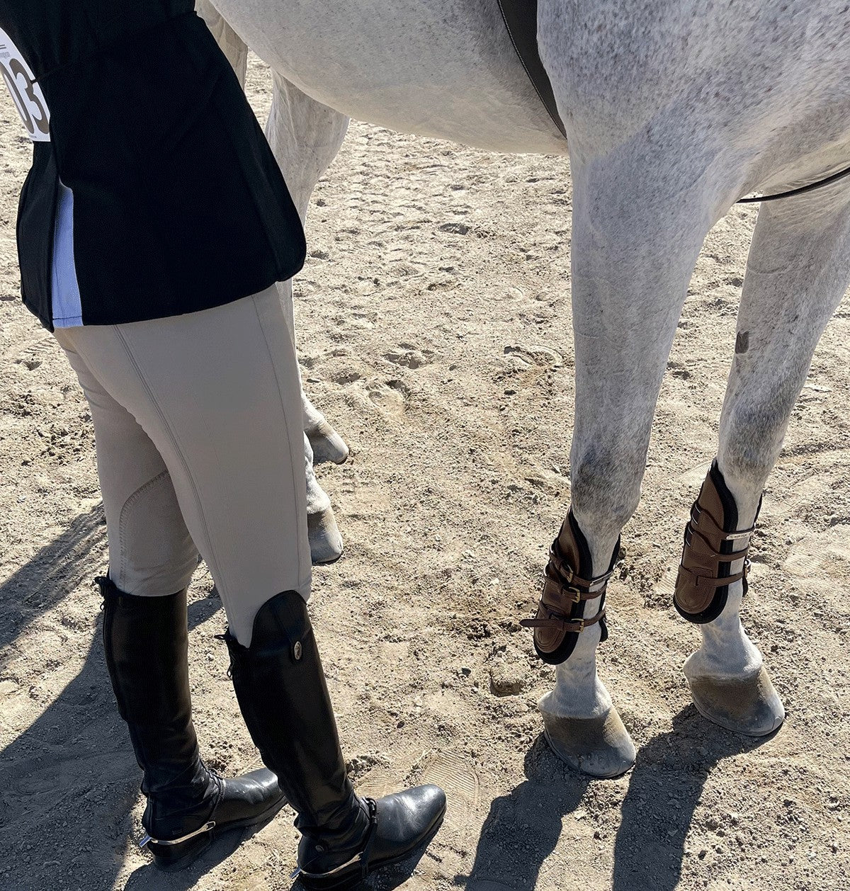 Angled front view of a gray horse wearing the havana Majyk Equipe 100% Leather Tendon Boots with Buckles while standing in the dirt