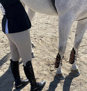 Angled front view of a gray horse wearing the havana Majyk Equipe 100% Leather Tendon Boots with Buckles while standing in the dirt
