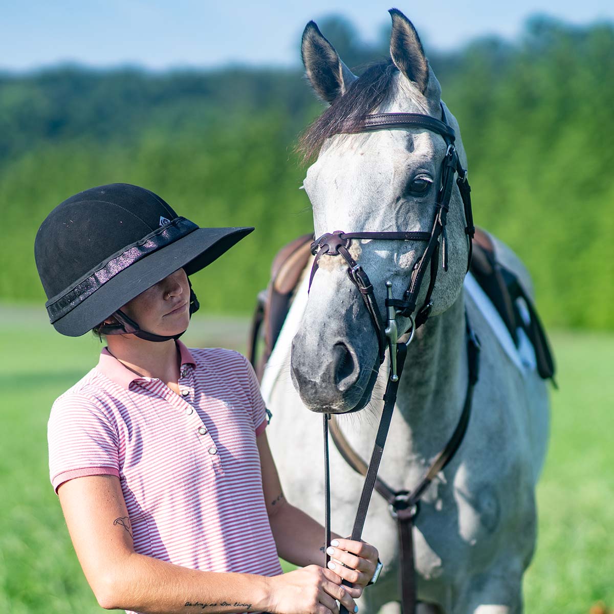 Angled front view of a rider wearing the midnight elegance EquiVisor Glitz Sun Visor while standing next to a gray horse outdoors