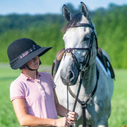 Angled front view of a rider wearing the midnight elegance EquiVisor Glitz Sun Visor while standing next to a gray horse outdoors