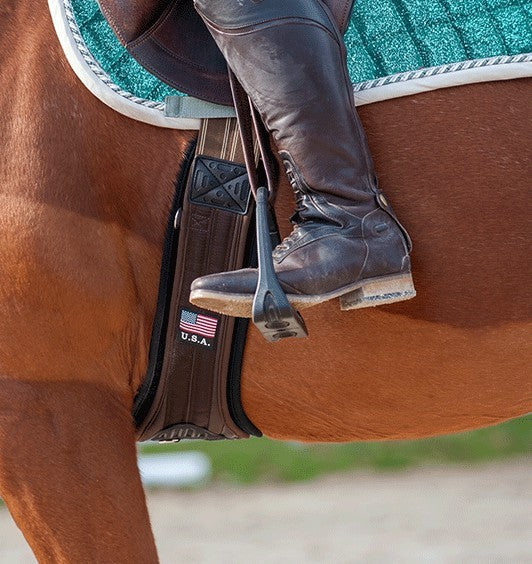 Side view of a horse wearing the brown Majyk Equipe Ergonomics EZ All Purpose Girth with a rider in the saddle