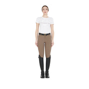 Full body view of a model wearing the Equestro Women's Slim Fit Grip Breeches With Logo in tan, white tshirt, and tall black boots on white background