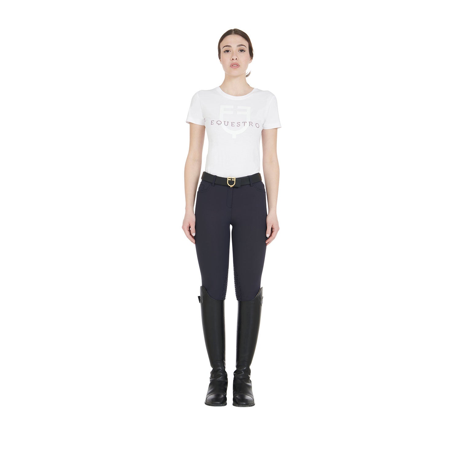 Full body view of a model wearing the Equestro Women's Slim Fit Grip Breeches With Logo in navy , a white tshirt, and black boots on white 