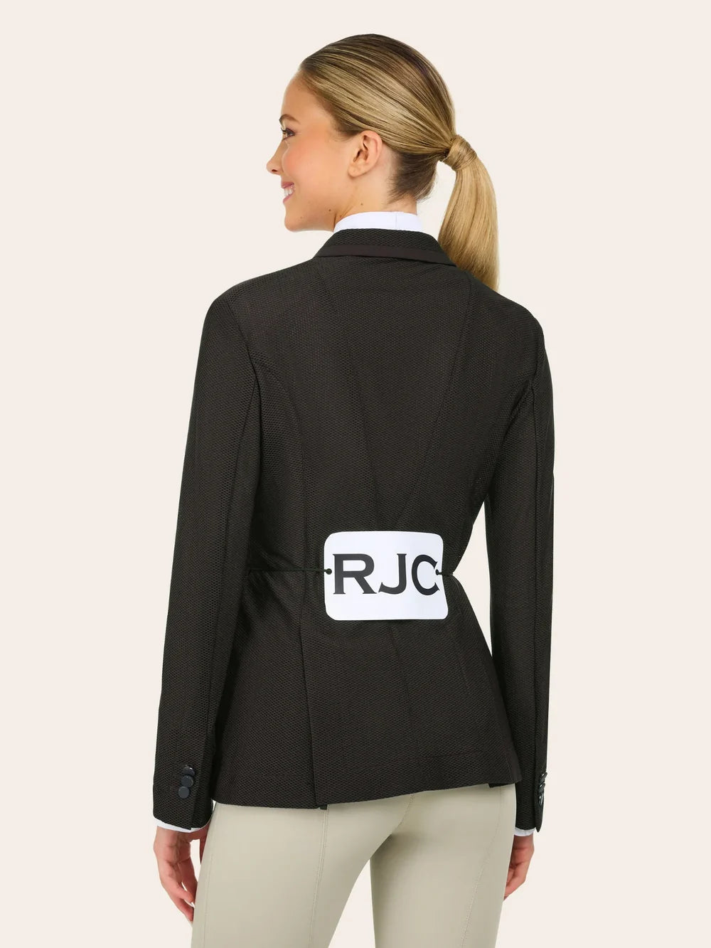 Back view of a woman wearing the brown RJ Classics Harmony Evo Mesh Show Coat with the letters RJC on a competition number holder on a plain background