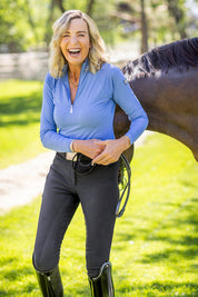 Front view of a female model wearing the Kastel Perforated Long Sleeve 1/4 Zip Base Layer while standing in front of a horse outdoors