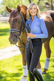 Front view of a female model wearing the Kastel Perforated Long Sleeve 1/4 Zip Base Layer while standing next to a horse outdoors