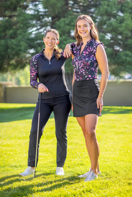 Front view of 2 female models wearing Black Begonia Kastel Shirts while standing in the grass outside