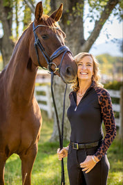 Front view of a model wearing the Espresso Leopard Kastel Long Sleeve Raglan 1/4 Zip Sun Shirt while standing outside next ot a chestnut horse